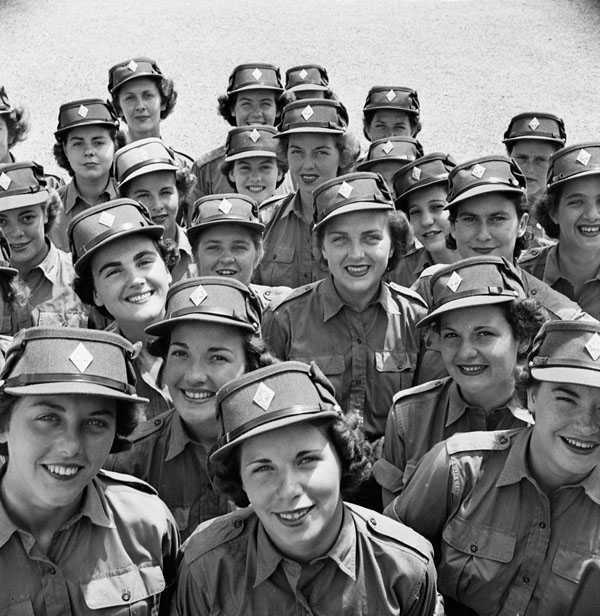 Black and white photograph. A large number of women smile up at the camera. Their faces are clearly visible, and they all wear the khaki cap of the Canadian Women's Army Corps.